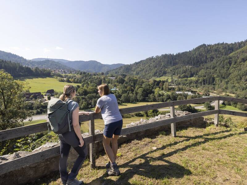 Zwei Wanderinnen stehen in der Sonne an der Schenkenburg und genießen die Aussicht über das Kinzigtal