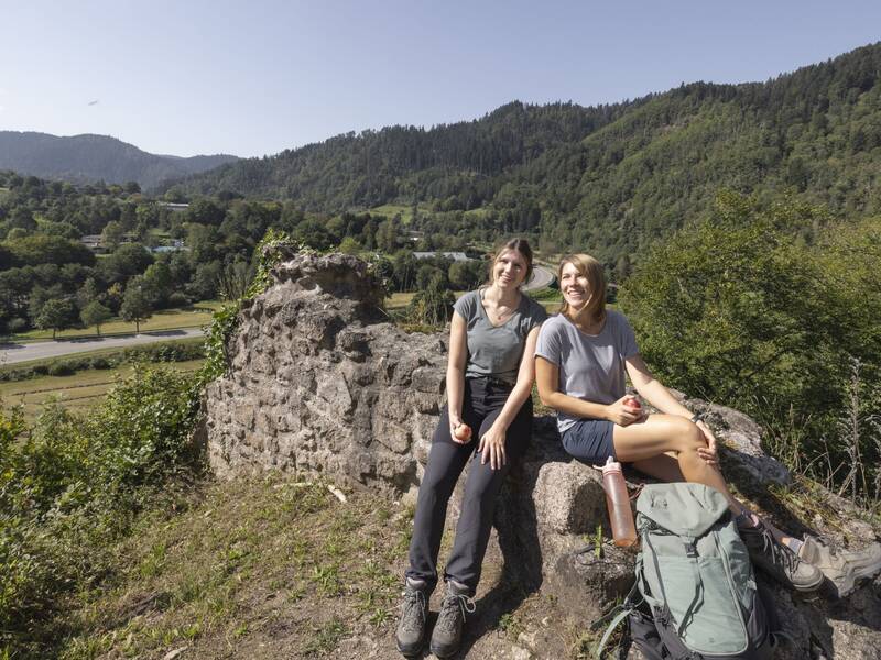 Zwei Wanderinnen machen in der Sonne a der Ruine Schenkenburg über dem Kinzigtal eine Pause