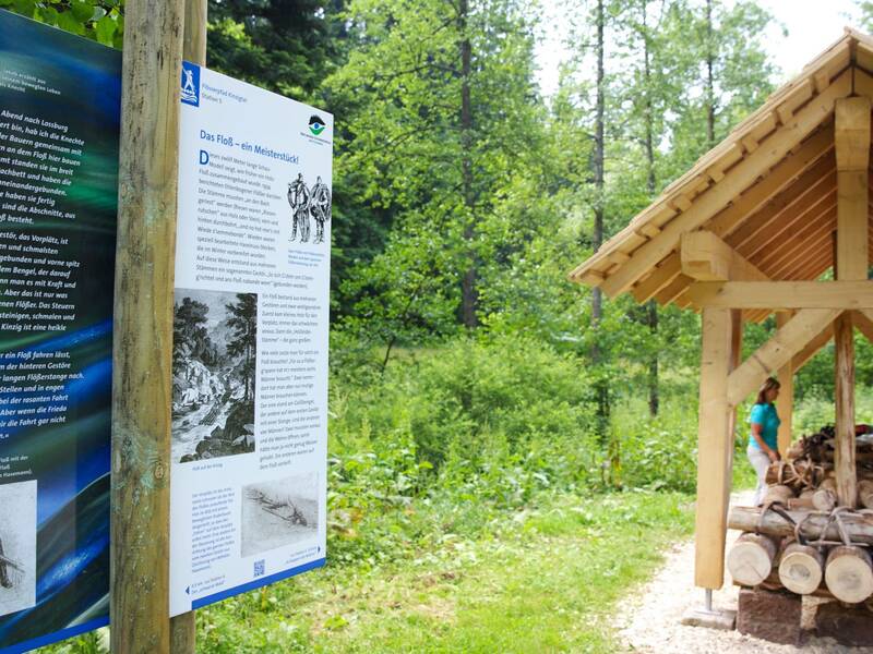 Originalgetreues überdachtes Schaufloß mit Infotafel und zwei Personen im Wald bei Ehlenbogen.