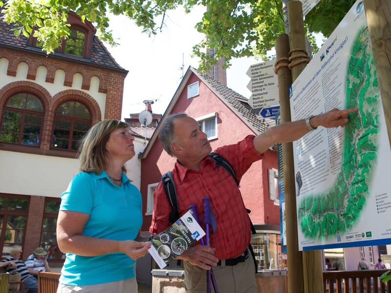 Ein Wanderpaar steht vor einer Infotafel des Flößerpfads in Alpirsbach.