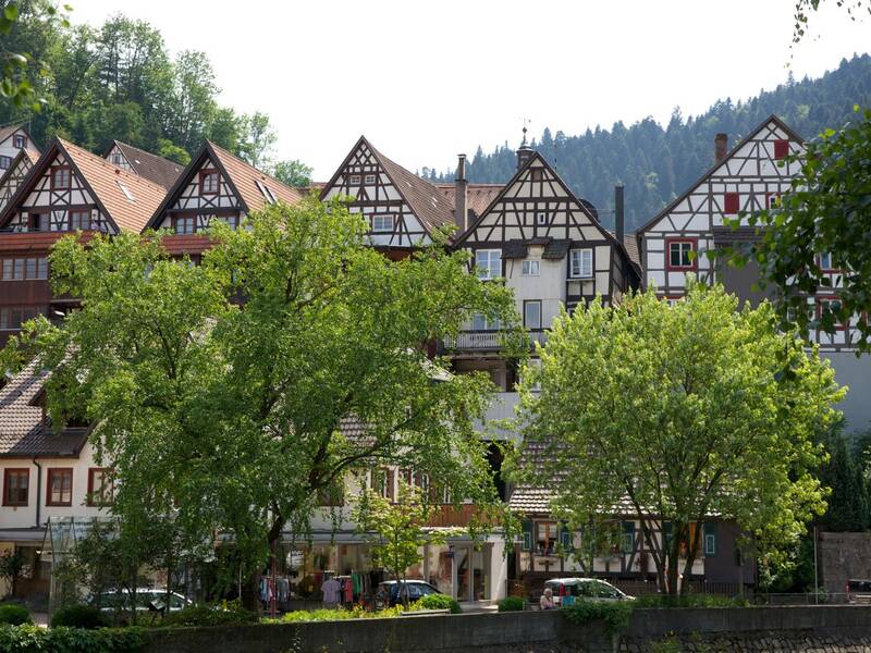 Ein Bild zeigt eine Reihe traditioneller, deutscher Fachwerkhäuser Am Ufer der Kinzig in Schiltach umgeben von grüner Vegetation.