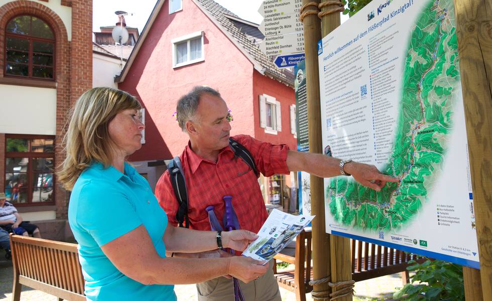 Zwei Wanderer betrachten aufmerksam eine Informationskarte im Freien.